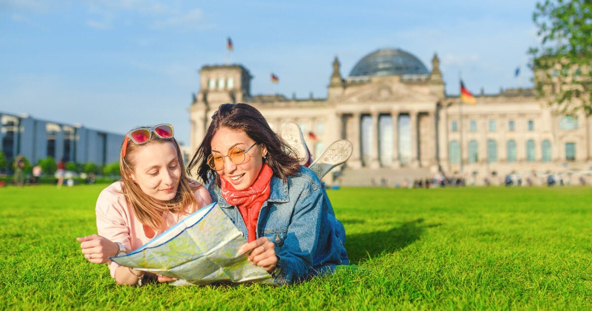 Duas jovens mulheres deitadas na grama, examinando um mapa, em um dia ensolarado e relaxante ao ar livre.