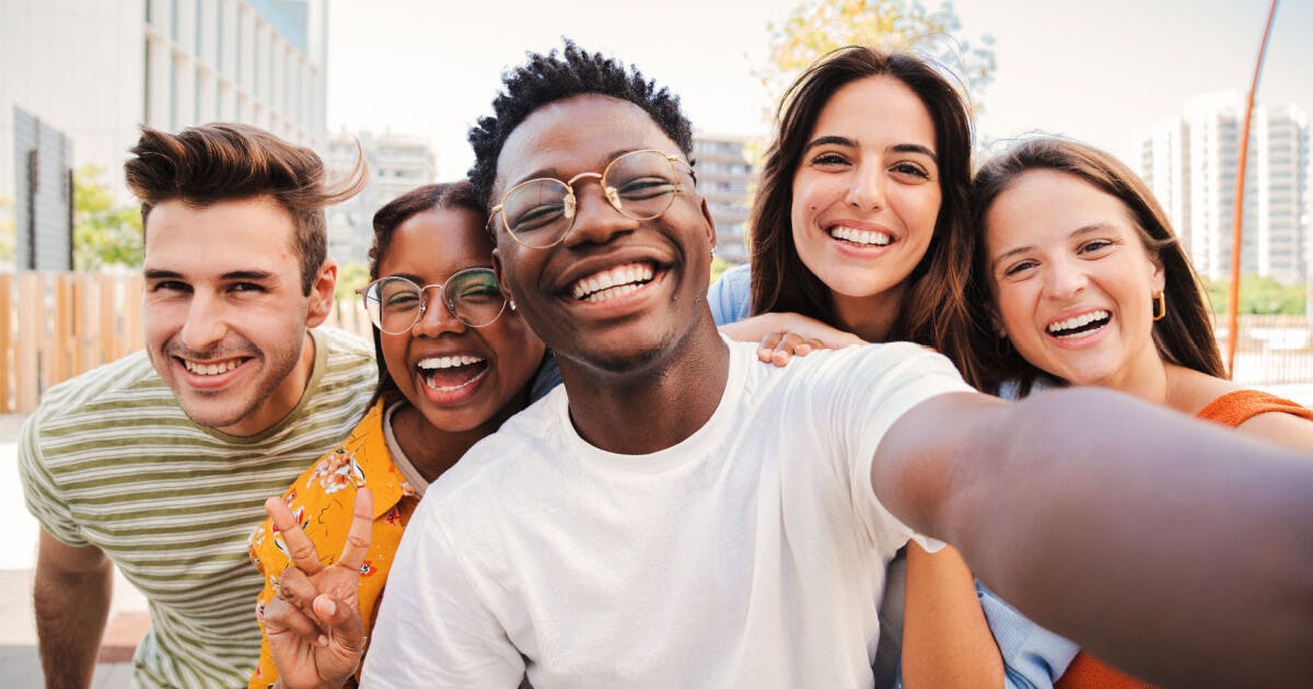 Grupo de jovens sorrindo e posando para uma selfie em um ambiente descontraído.