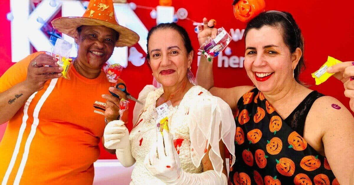 Três mulheres sorrindo e com fantasias temáticas de Halloween.