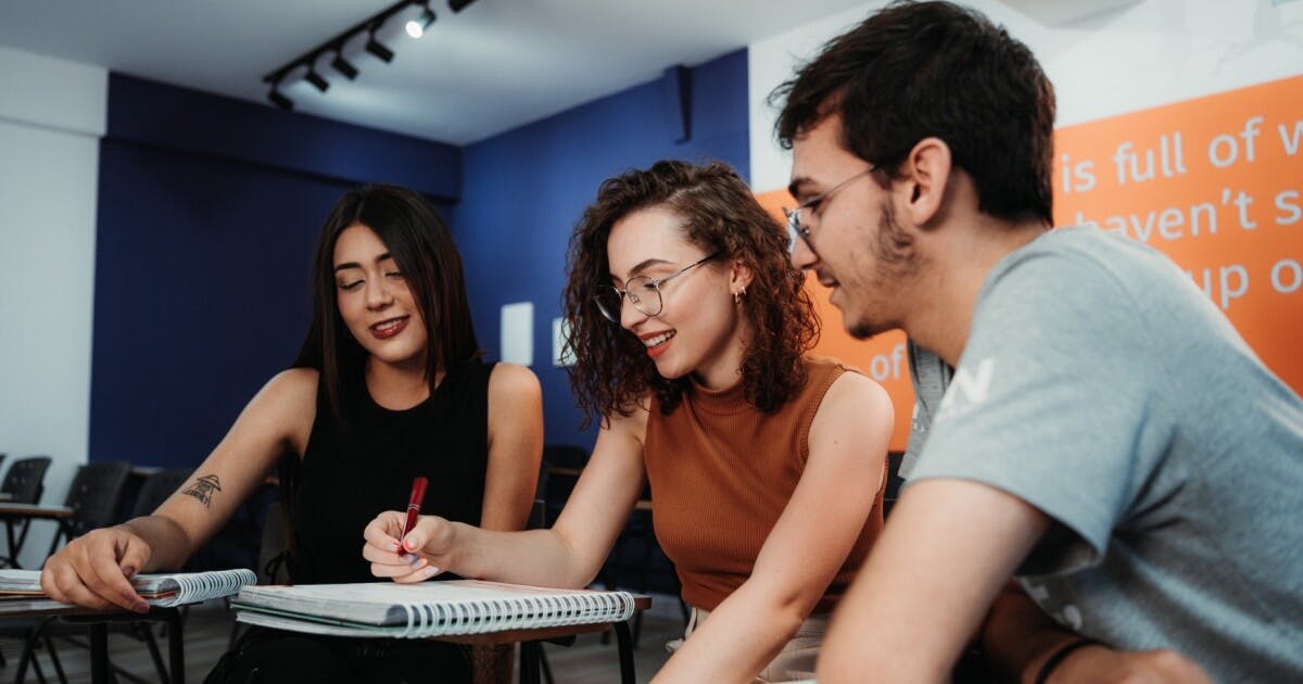 três alunos olhando para um livro de idiomas na sala de aula