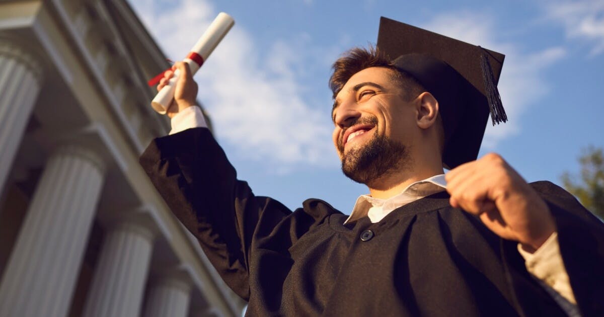 Aluno sorrindo com o canudo do diploma na mão e levantando para o alto