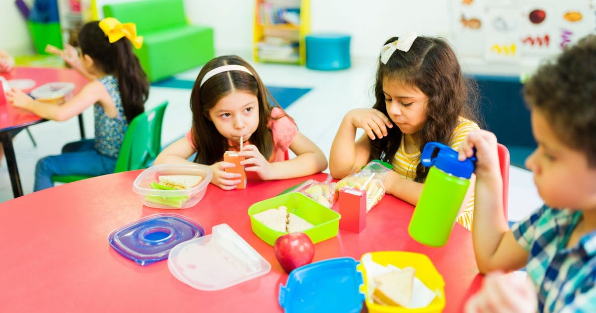 Crianças fazendo lanche na mesa de uma sala de aula.