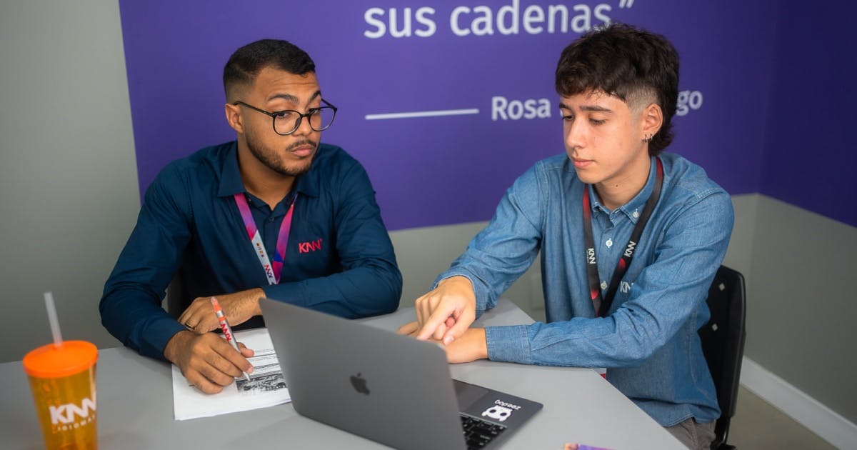 Dois colaboradores da franquia KNN conversando e olhando para um Macbook.