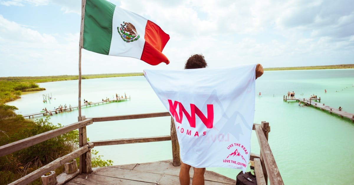 Pessoa com a bandeira da KNN Idiomas enrolada nas costas e ao lado uma bandeira do México.