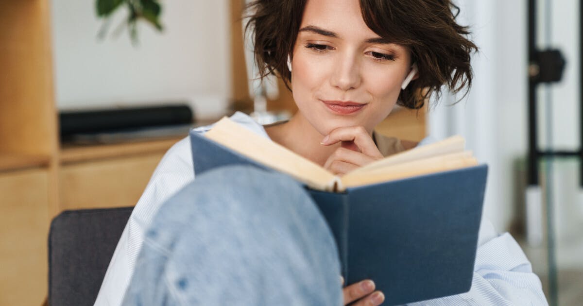 Mulher lendo um livro enquanto está sentada em um sofá confortável.