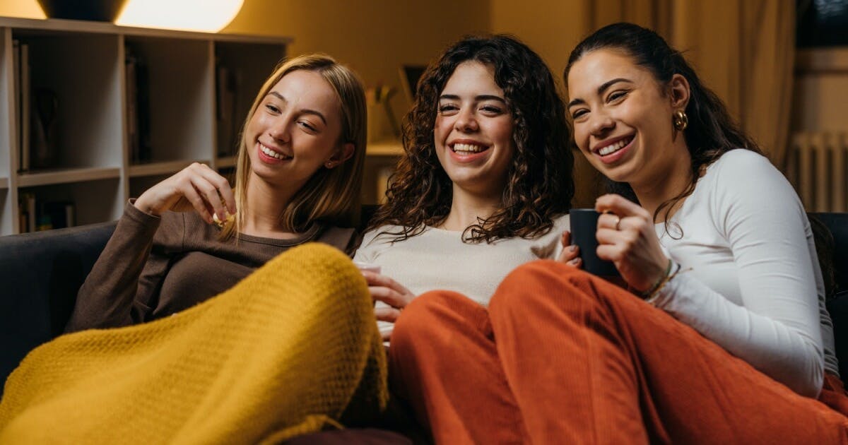 Três mulheres sentadas em um sofá, sorrindo e rindo juntas, transmitindo alegria e amizade.