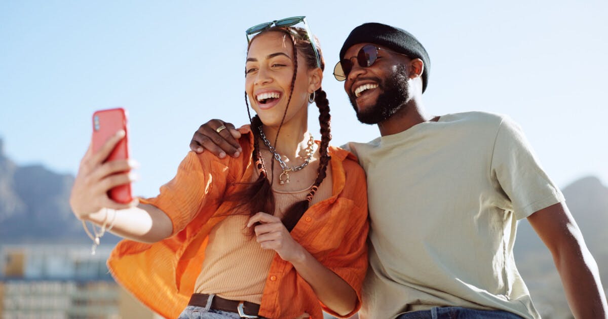 Casal sorridente tirando uma selfie com um celular, capturando um momento especial juntos.