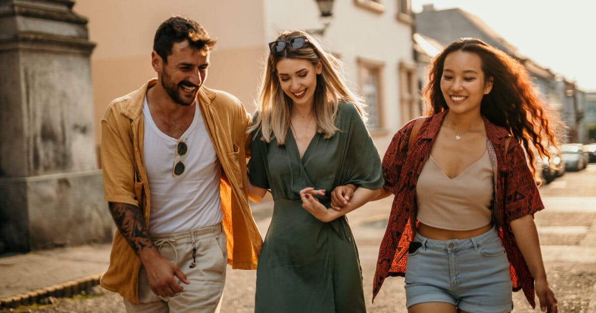 Três amigos caminhando juntos pela rua, sorrindo e desfrutando de um momento de amizade e companheirismo.