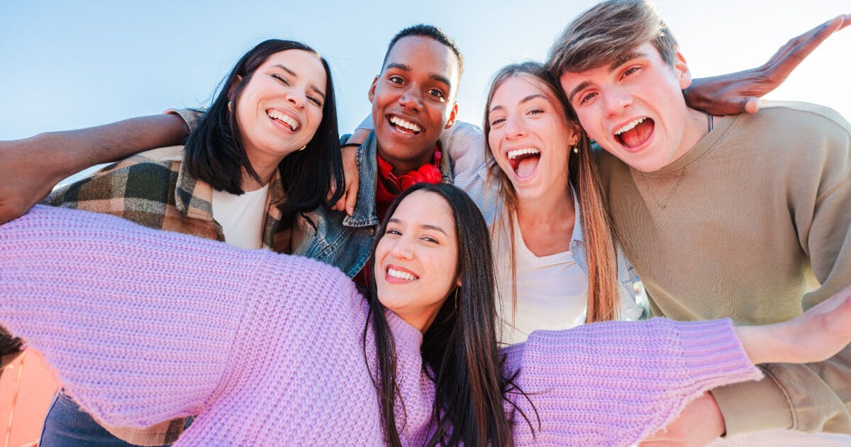 Grupo de jovens sorrindo e tirando uma selfie, capturando um momento de alegria e amizade.