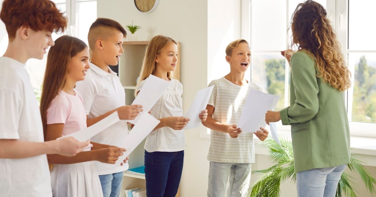 Professora ensaiando música com crianças e todos com uma folha de papel na mão.