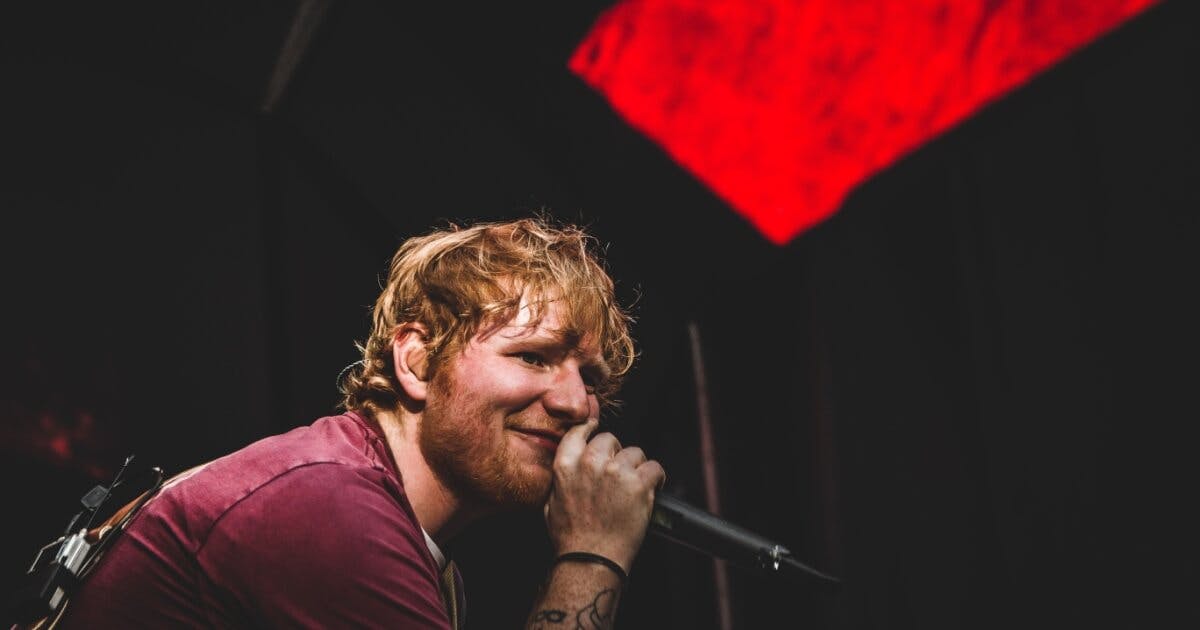 Cantor Ed Sheeran olhando para plateia e com microfone na mão.