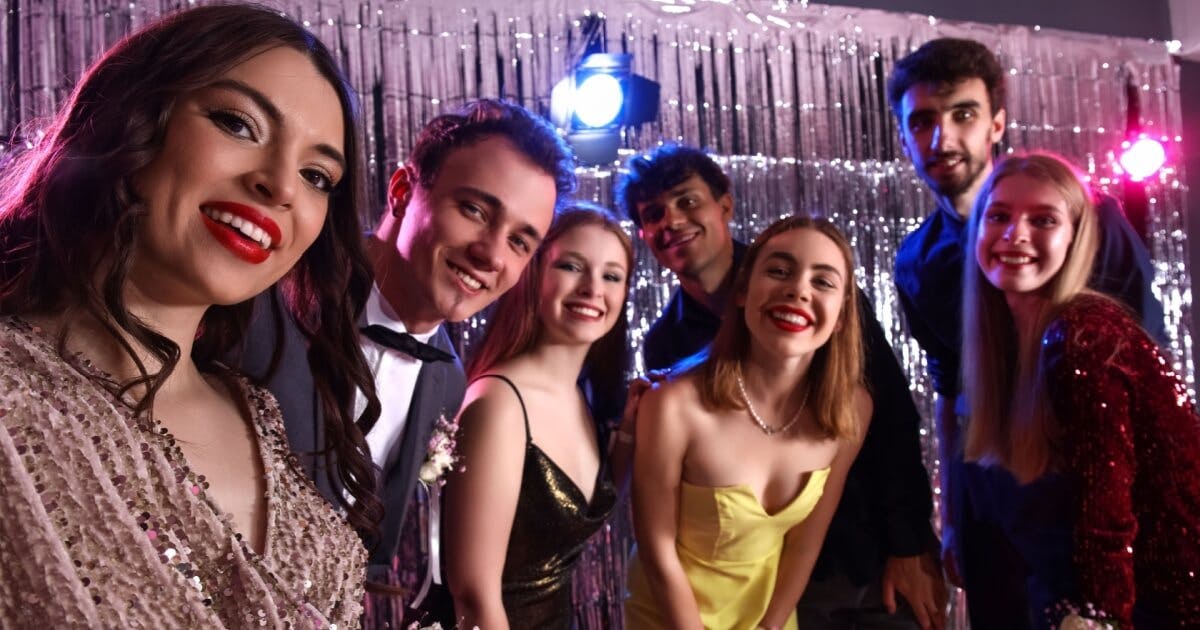 Quatro mulheres e três homens sorrindo para uma foto selfie e com roupas de festa.