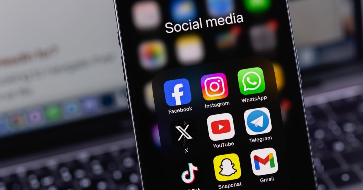 Imagem de um celular (iPhone) mostrando alguns aplicativos de redes sociais, como: Facebook, Instagram, WhatsApp,X, Tiktok, entre outros.