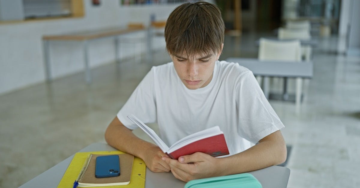 Jovem aluno sentado em uma sala de aula sozinho e lendo um livro.