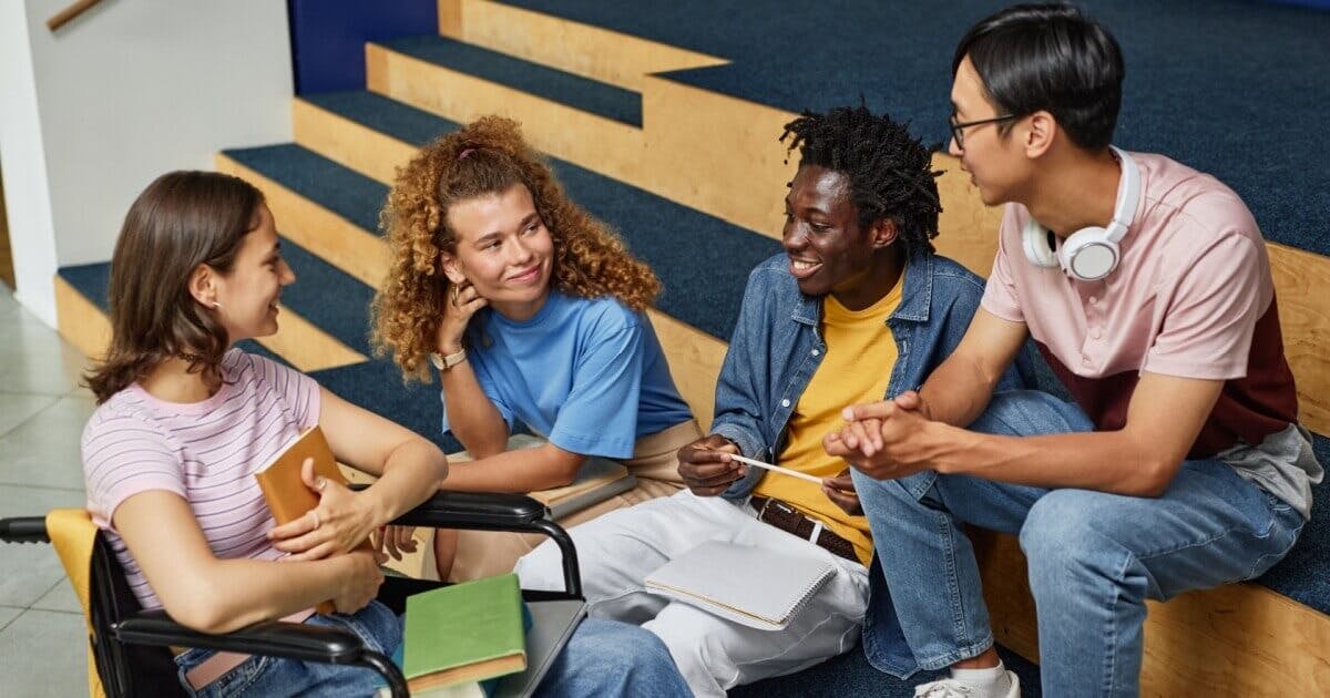 4 alunos (duas mulheres e dois homens) conversando e sorrindo.