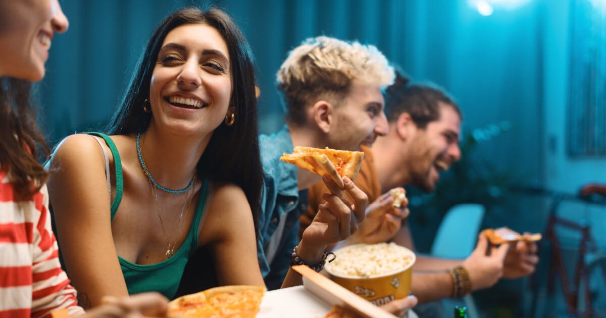 Grupo de pessoas reunidas, saboreando pizza enquanto assistem a um filme, criando um ambiente de confraternização e diversão.