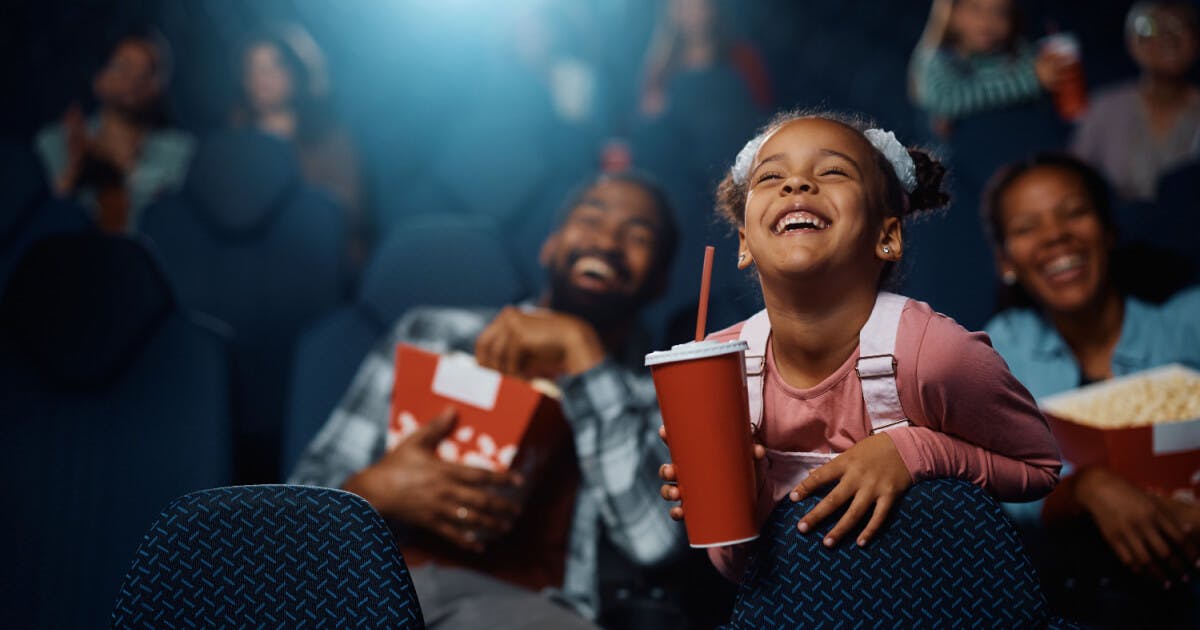 Menina sorridente assistindo a um filme no cinema, expressando alegria e encantamento.