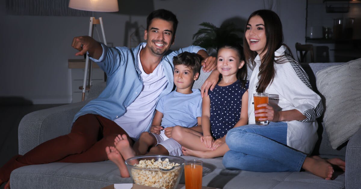 Uma família sentada no sofá, desfrutando de bebidas e pipoca, compartilhando momentos de alegria e descontração.