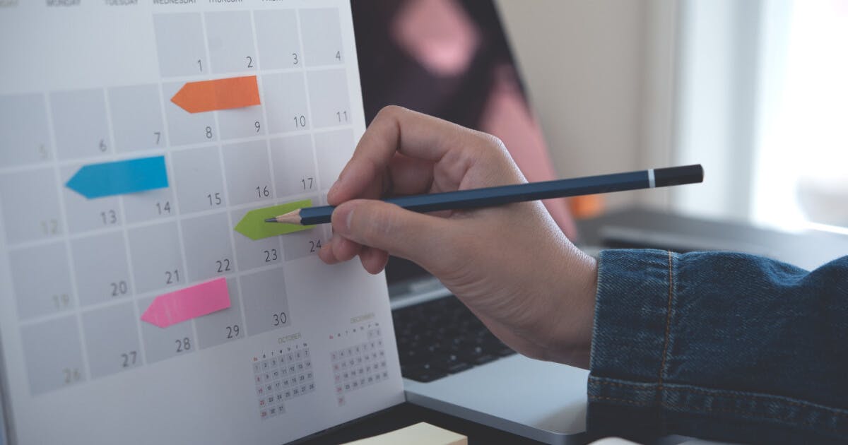 Mão anotando em um calendário.