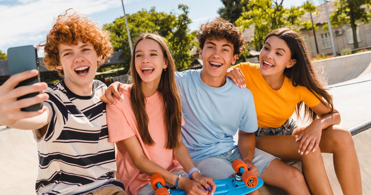 Quatro amigos tirando uma selfie com seus skates, sorrindo e se divertindo em um ambiente ao ar livre.