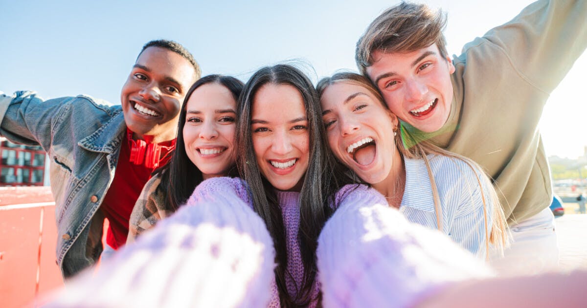 Cinco jovens sorrindo e posando juntos para uma selfie, capturando um momento de amizade e diversão.