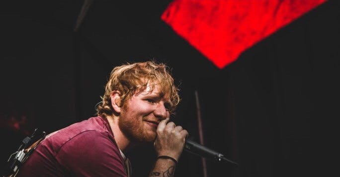 Cantor Ed Sheeran com o microfone na mão, em cima do palco.