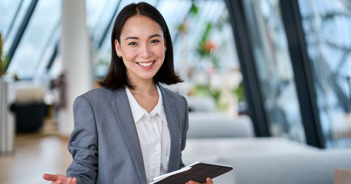 Uma empresária asiática segurando uma prancheta e sorrindo, transmitindo confiança e profissionalismo.