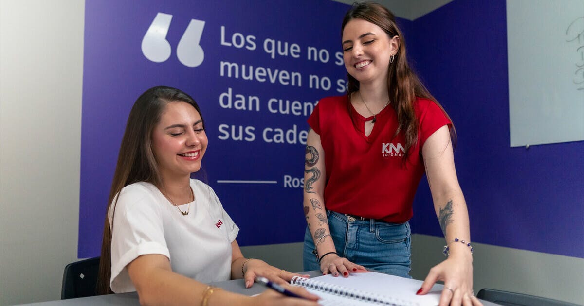 Duas mulheres sentadas à mesa, escrevendo com uma caneta em um papel.