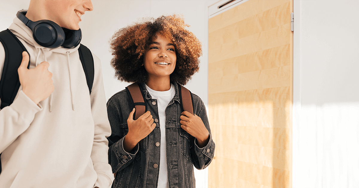 Um homem e uma mulher em pé diante de uma porta, ambos sorrindo e aparentando estar em uma conversa amigável.