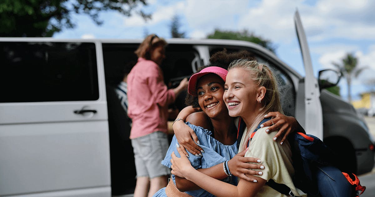 Duas jovens mulheres se abraçando em frente a uma van, transmitindo alegria e amizade.