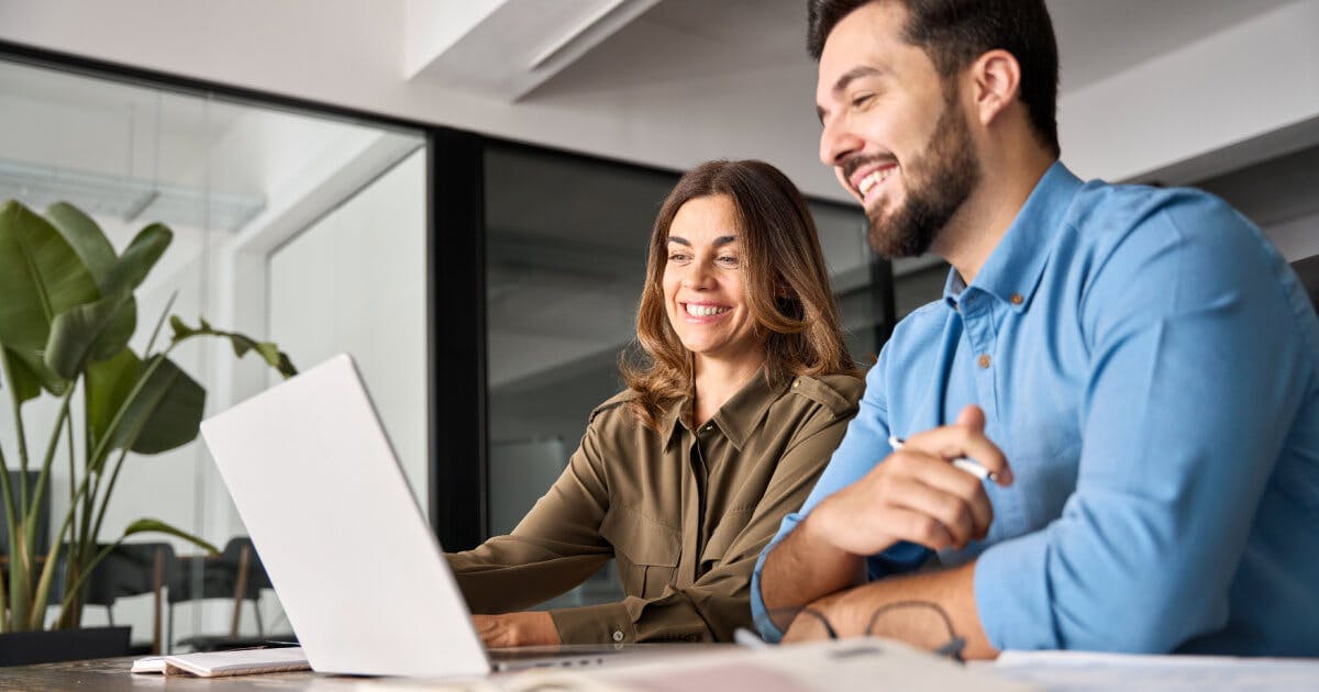 Um homem e uma mulher sorriem enquanto trabalham juntos em um laptop.