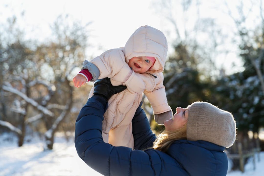 mamma lyfter upp bebis i overall utomhus på vintern