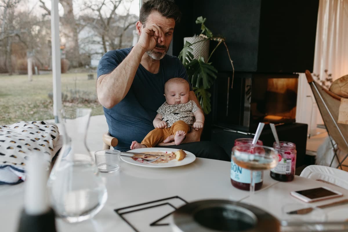 trött pappa med bebis i knät vid frukostbordet