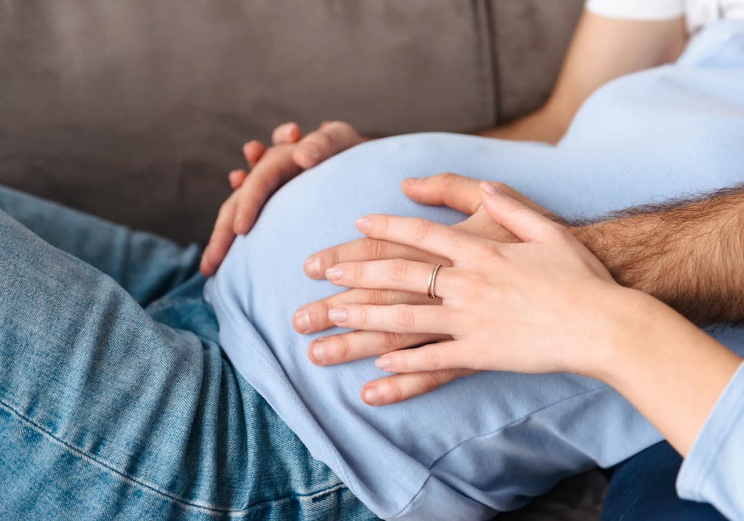 Kvinna och man som håller om kvinnans gravidmage