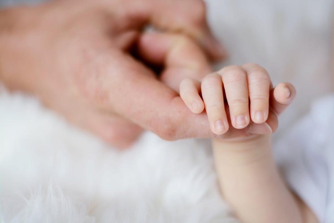 Lite bebis som håller om finger på vuxen