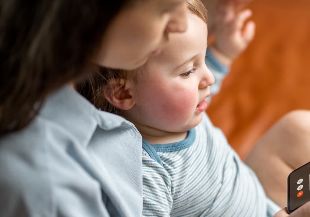 barn med rosiga kinder som sitter i knä på mamma