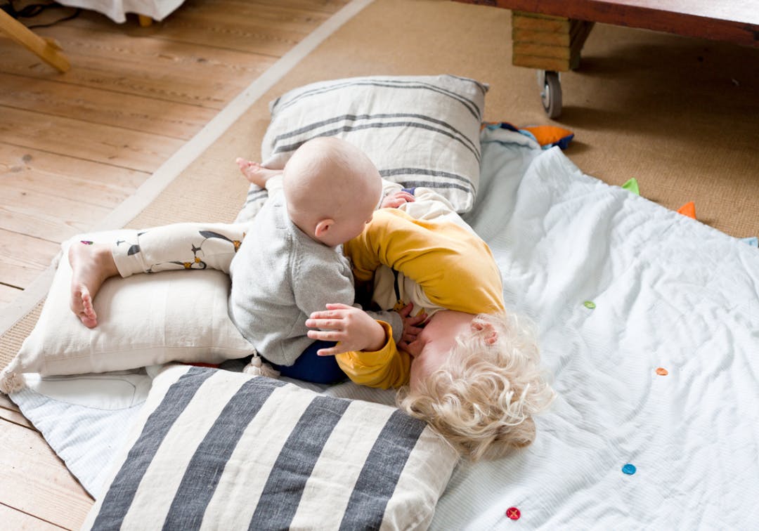 två syskon leker på en filt på golvet