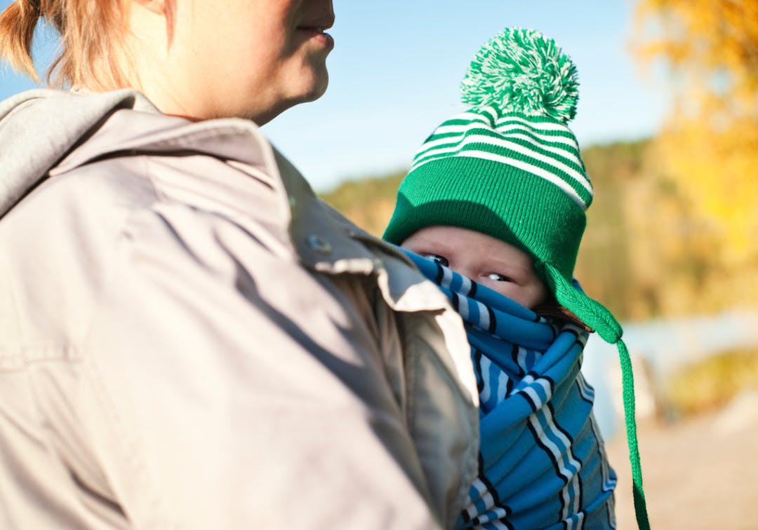 Närbild på mamma med barn i bärsjal ute på hösten