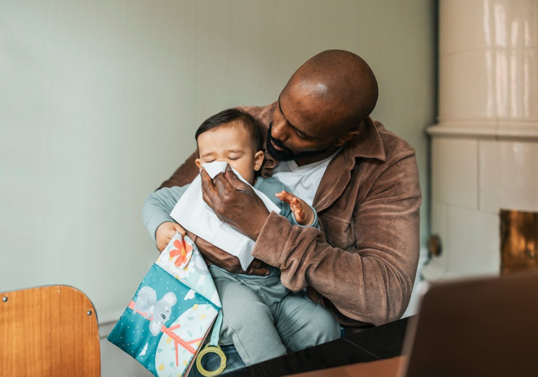 pappa snyter sitt förkylda småbarn som sitter i hans knä.