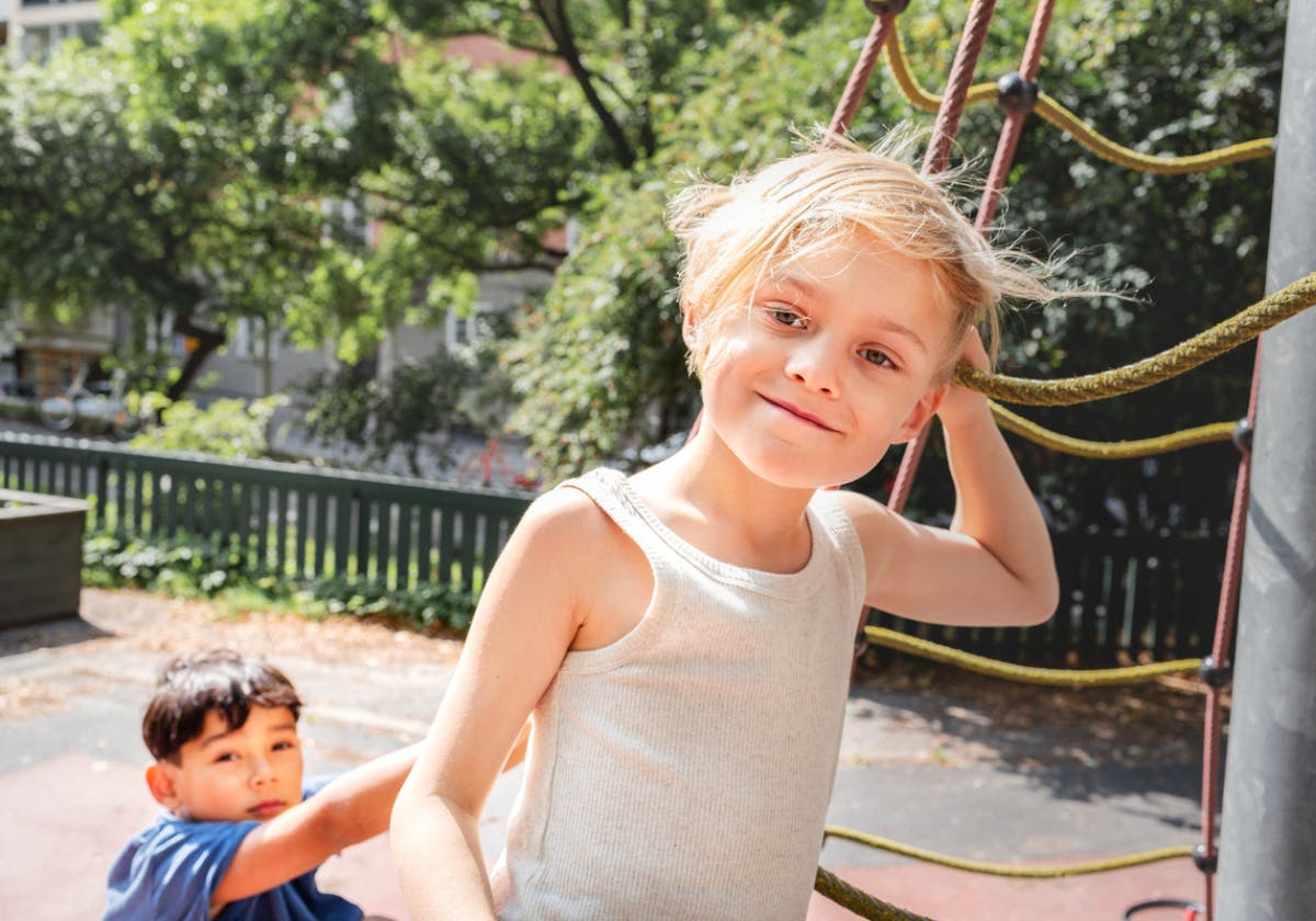 Barn som klättrar i ett klätternät på en lekplats och ser nöjd ut medan ett annat barn står bakom.