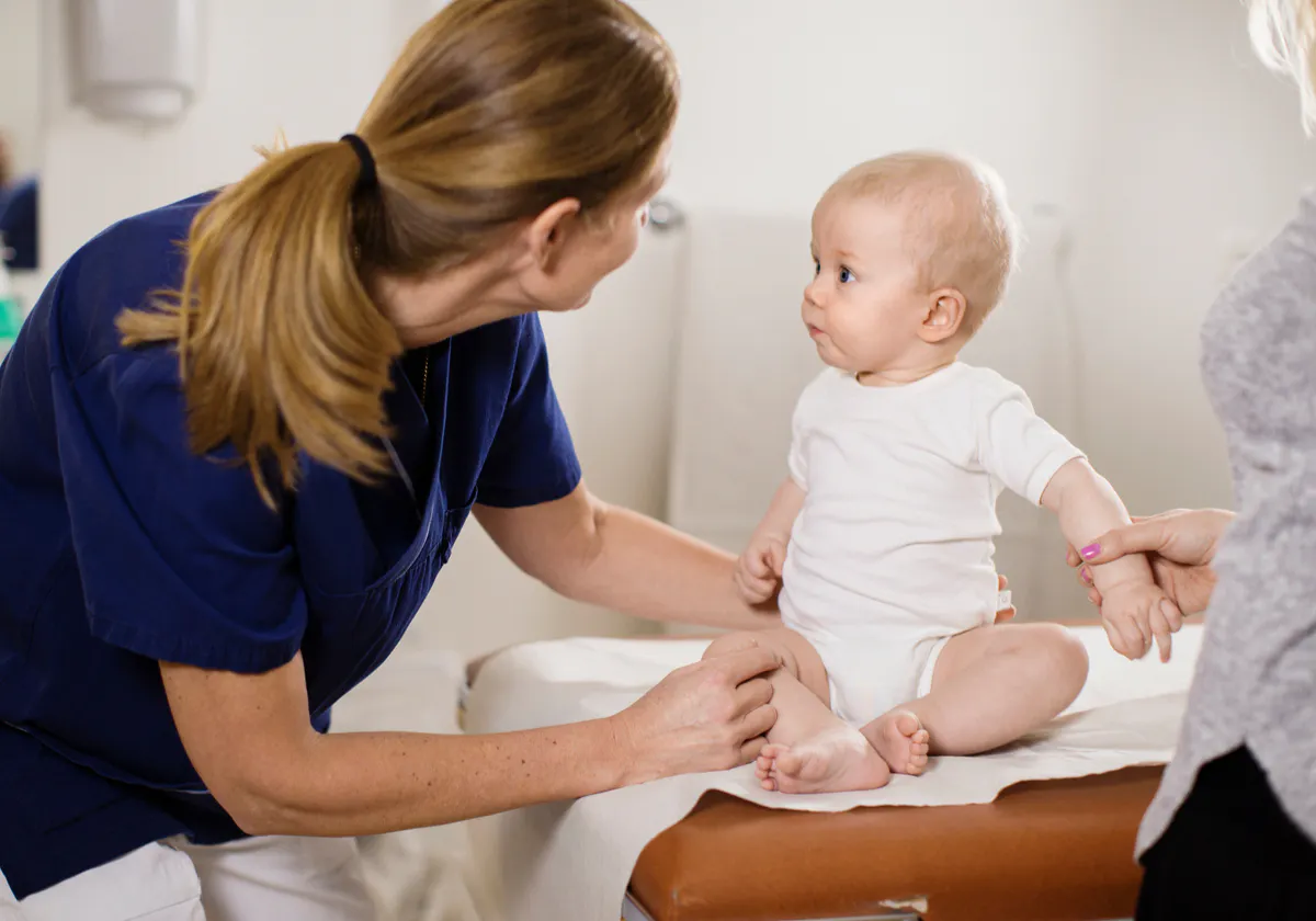 barnsjuksköterska och litet barn sittandes på brits i ett undersökningsrum tittar på varandra