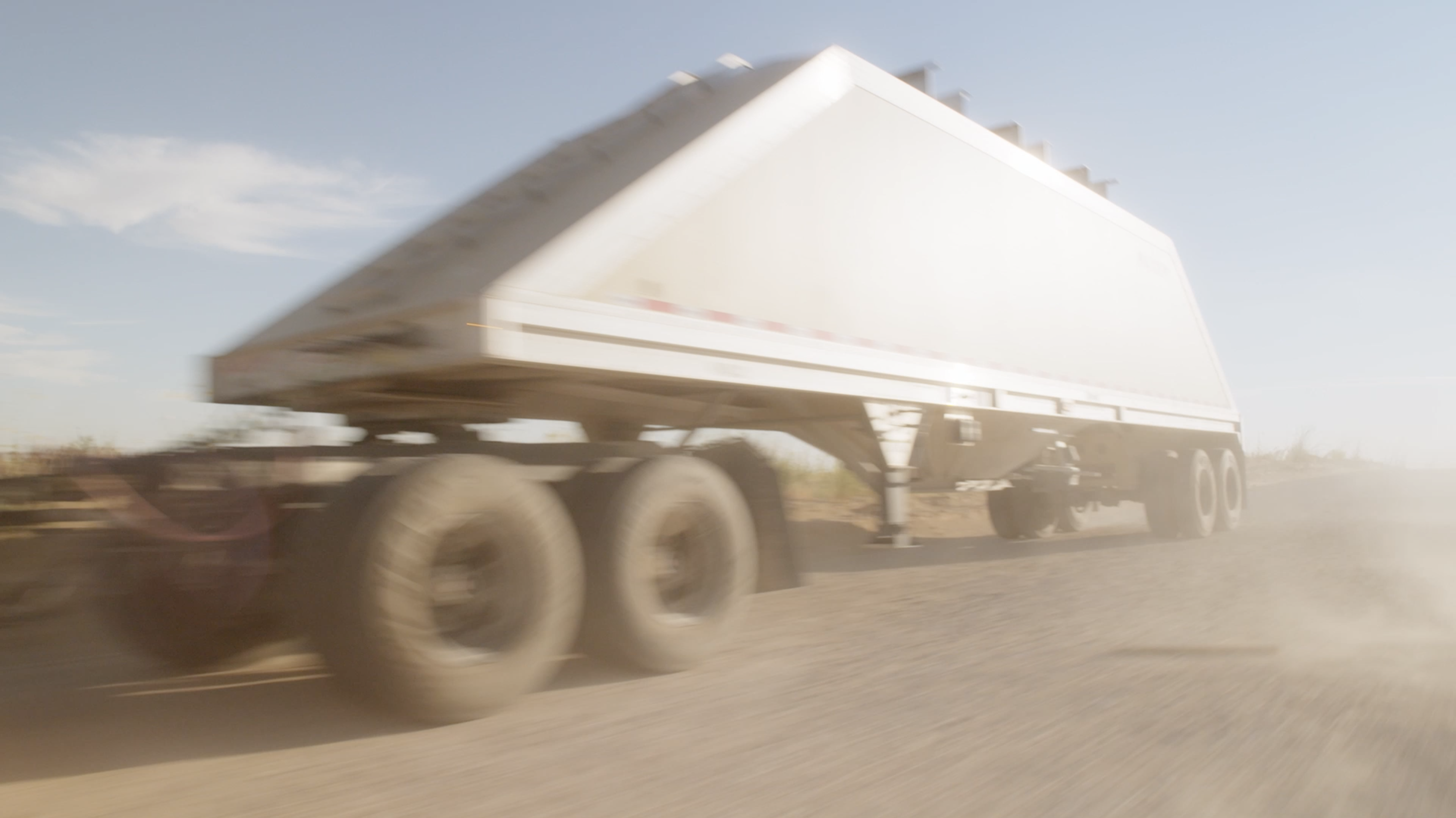 Side view of a Kodiak truck pulling a hopper trailer on a dirt road
