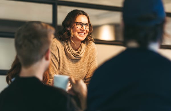 ledningsgrupp man ser en kvinna i gul tröja som står böjd över bordet och pratar med gruppen