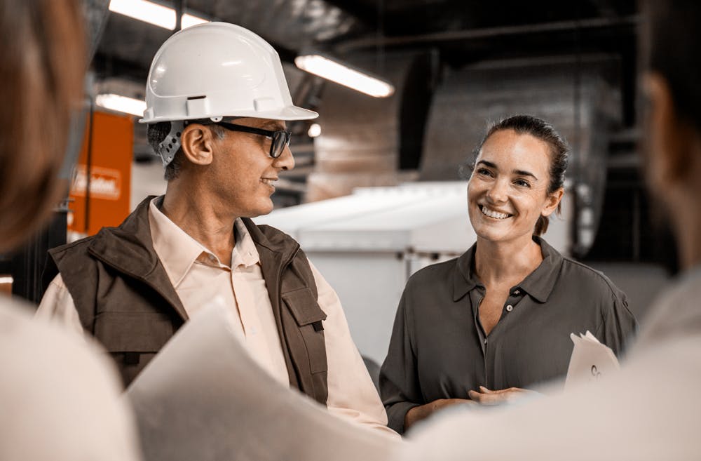 industrilokal-man-i-hjalm-och-kvinna-kontorskladd-diskuterar