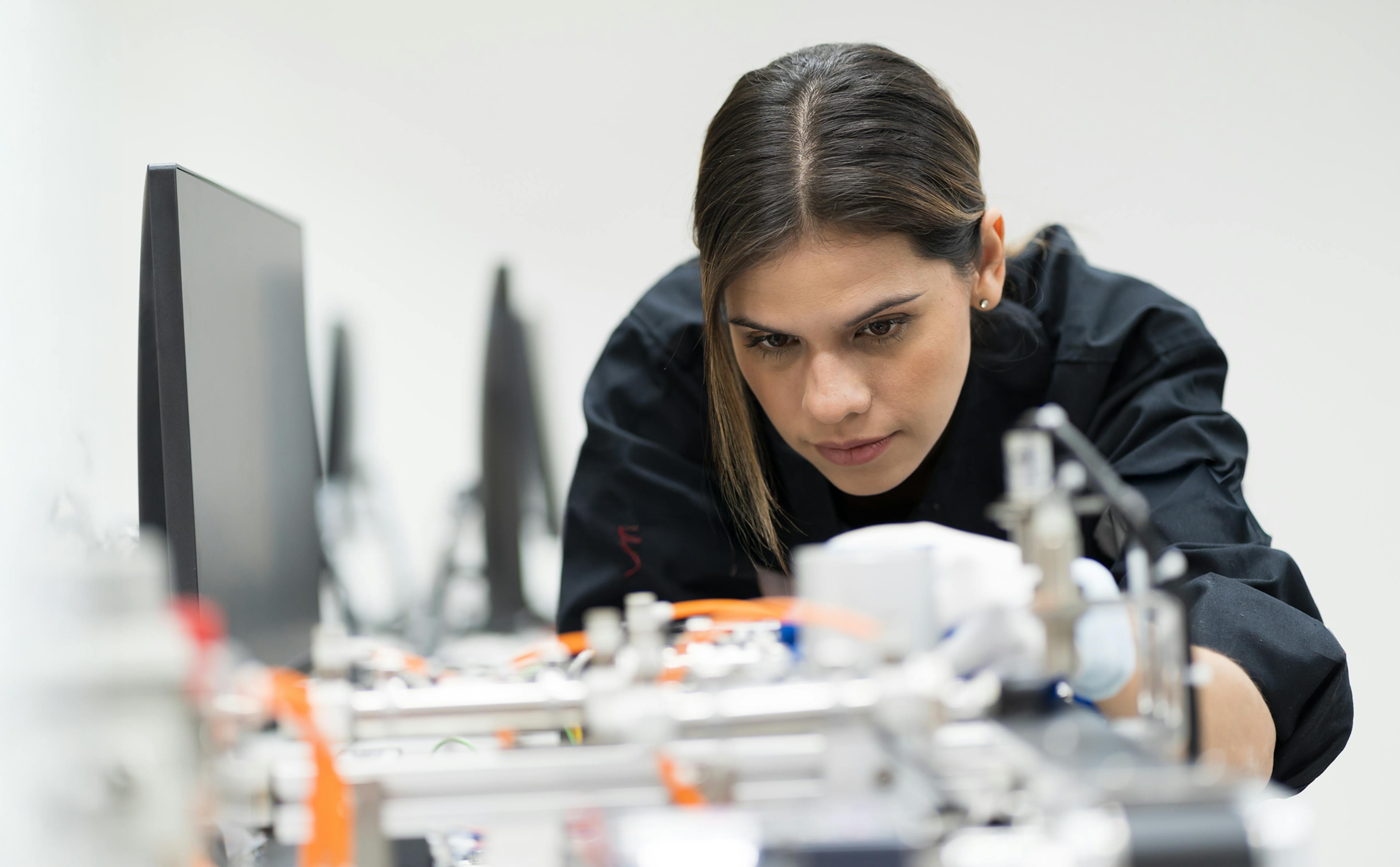 tjej står böjd och koncentrerad över elektriska prylar

