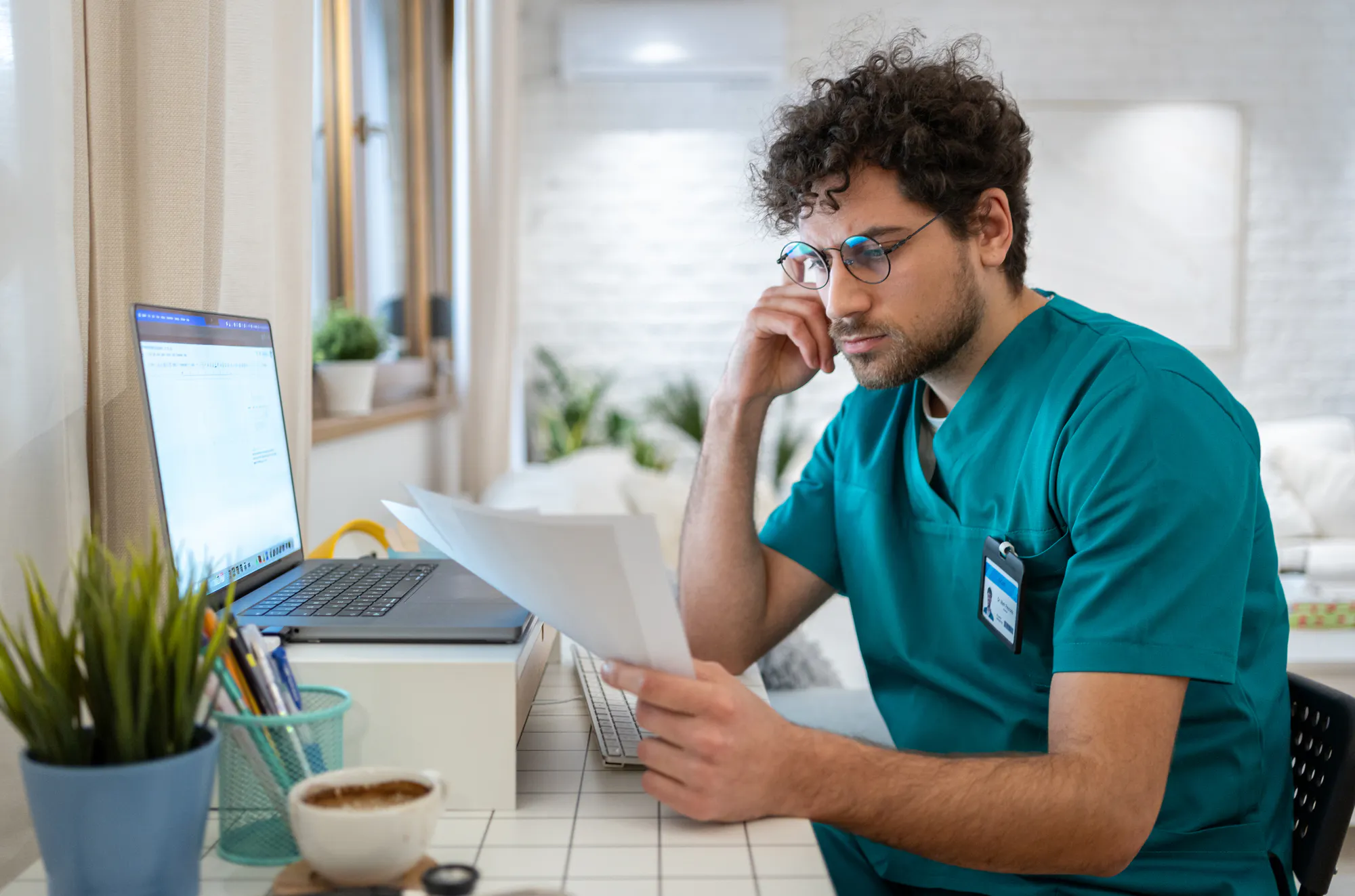 man-i-sjukhusklader-pluggar-vid-dator-kollar-pa-papper