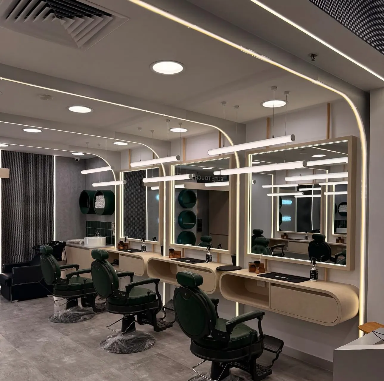 Barbershop stations featuring curved ceiling LED light strips and hanging linear pendant lights.