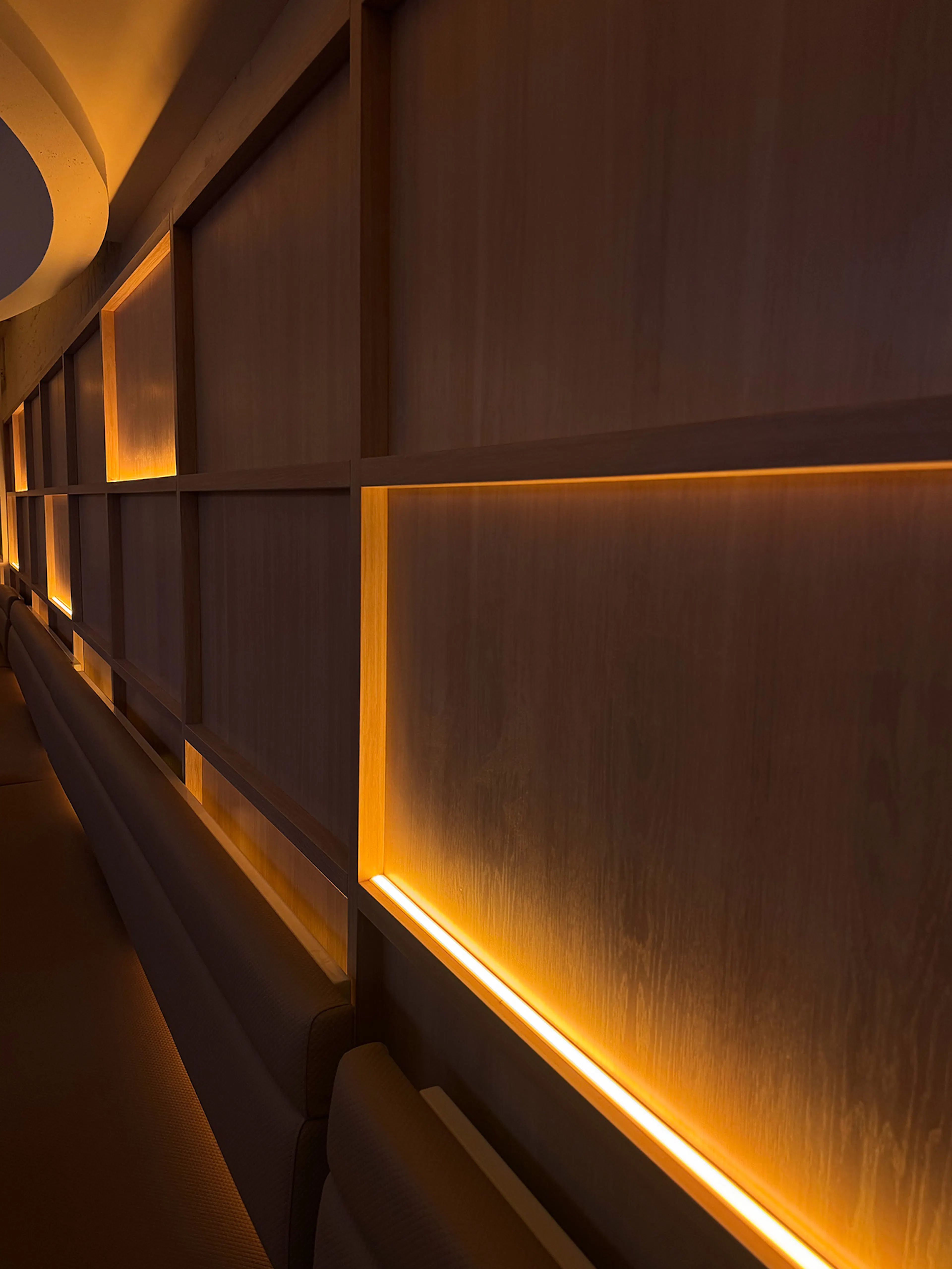 Custom wooden wall panelling with integrated warm LED linear cove lighting along booth seating