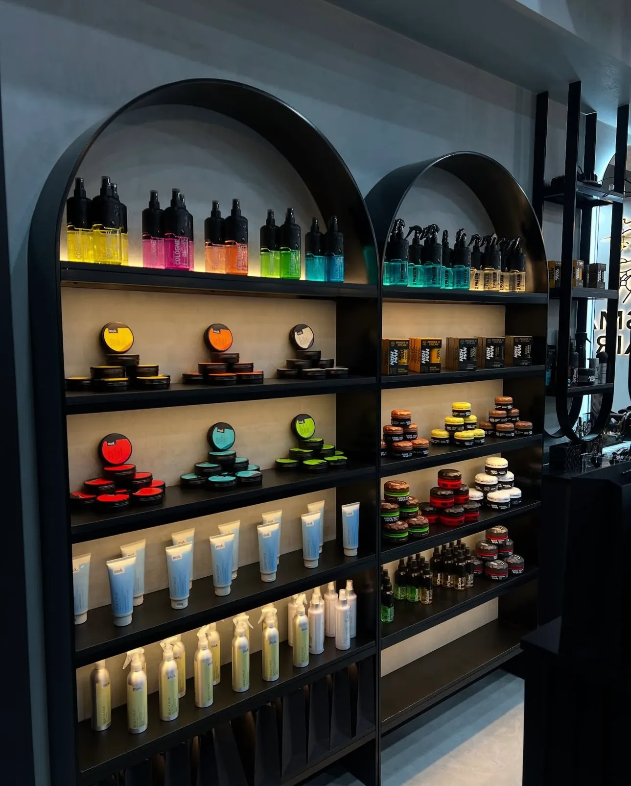 Arched black retail display shelving illuminated by warm LED strip lights beneath each shelf.