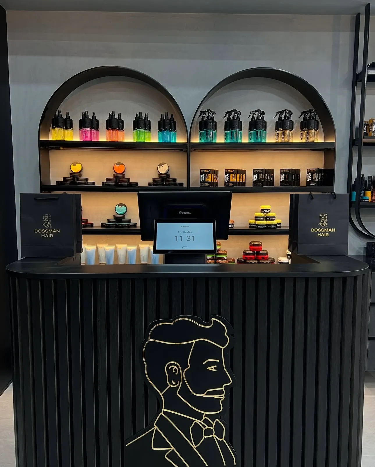 Front reception desk with a gold logo motif in front of warm backlit arched product shelves.